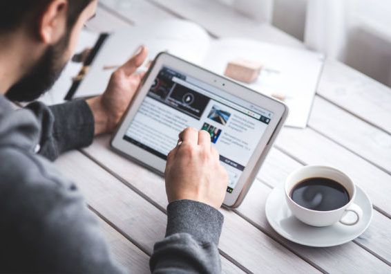 Mann sitzt mit einer Tasse Kaffee an seinem Tablet und surft im Internet