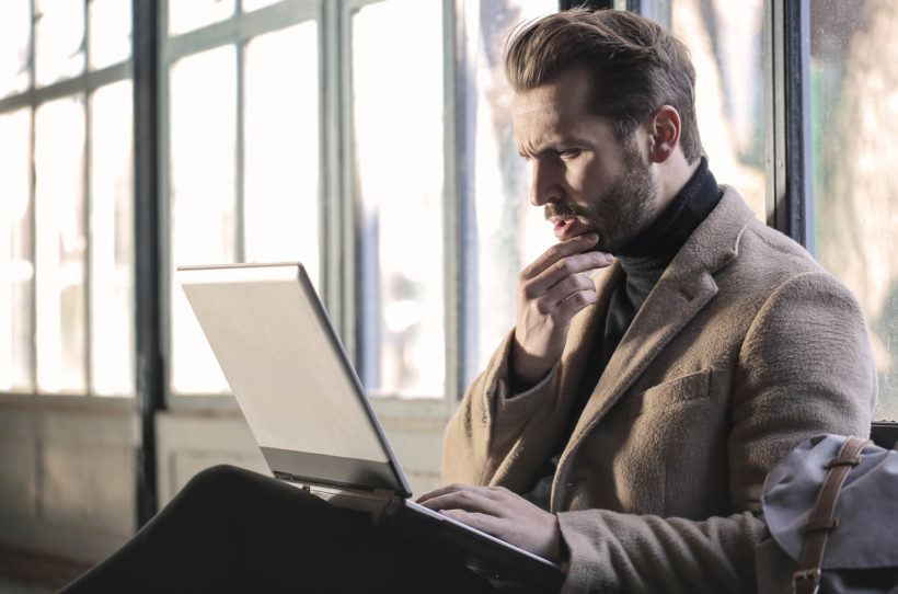 Man with Coat thinking about a Grey Laptop