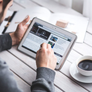 Mann sitzt mit einer Tasse Kaffee an seinem Tablet und surft im Internet