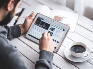 Mann sitzt mit einer Tasse Kaffee an seinem Tablet und surft im Internet