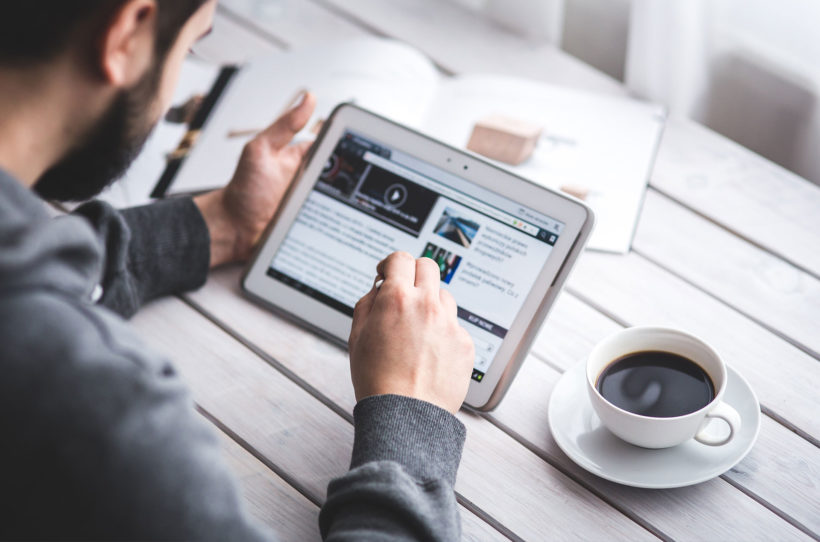 Mann sitzt mit einer Tasse Kaffee an seinem Tablet und surft im Internet